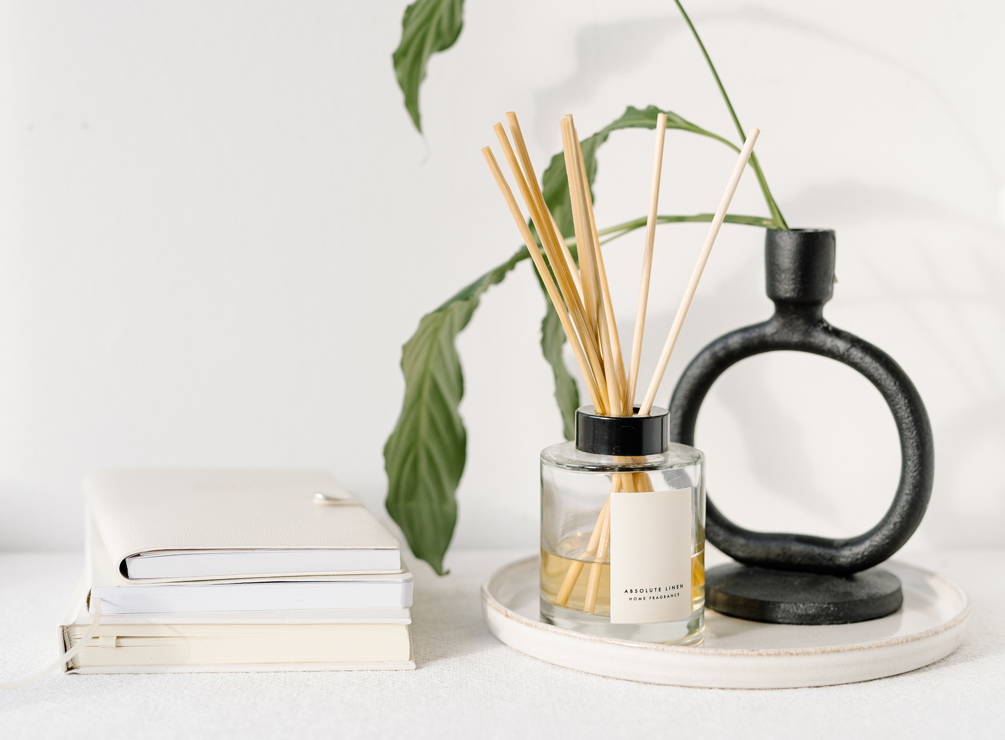 A white background with a stylish black vase and oil difuser along side books and work items